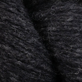 Close-up image of Patagonia Organic Merino by Juniper Moon Farm yarn with a textured, slightly fuzzy appearance. The dark gray-black fibers appear soft, and light gray strands interspersed throughout add a subtle pattern to the overall look. Made from GOTS certified organic Merino wool by Knitting Fever / Euro Yarns, it's perfect for your next eco-friendly project.