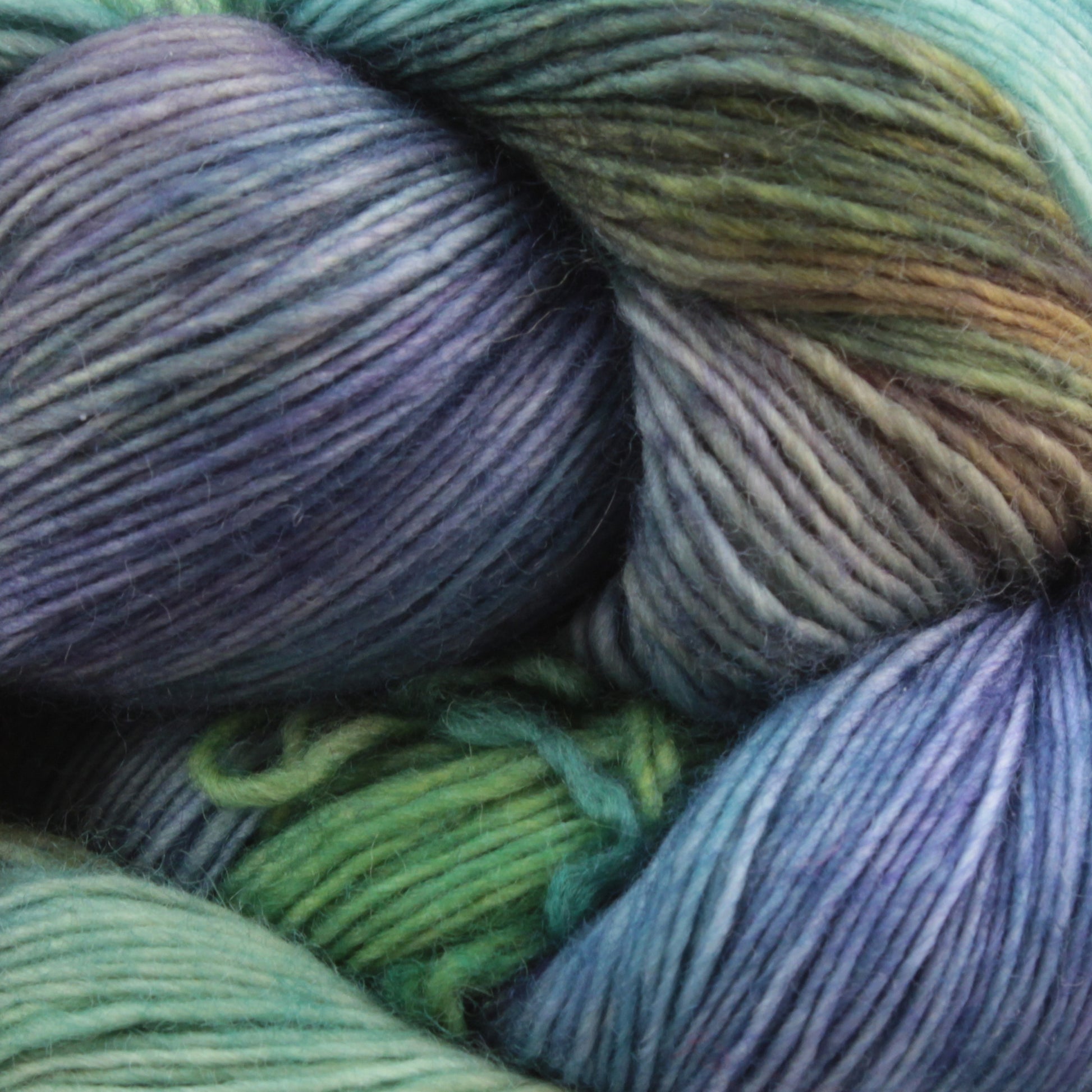 A close-up view of softly twisted multicolored Malabrigo Lace yarn by Malabrigo Yarn. This merino wool yarn showcases shades of blue, green, and purple blending seamlessly together, creating a soothing gradient effect. The texture appears soft and smooth, making it ideal for knitting or crocheting projects like delicate knitted shawls.