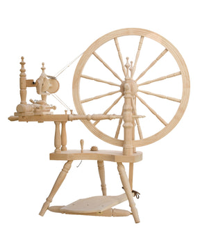 The Kromski Polonaise Spinning Wheel from Kromski North America is a traditional spinning wheel crafted from European alder and birch. It features a large wheel on the right side and includes components such as spindles, a thread guide, and a treadle pedal. The light wood has a smooth, polished finish with intricate turned details, offering both double drive and scotch tensioning options.