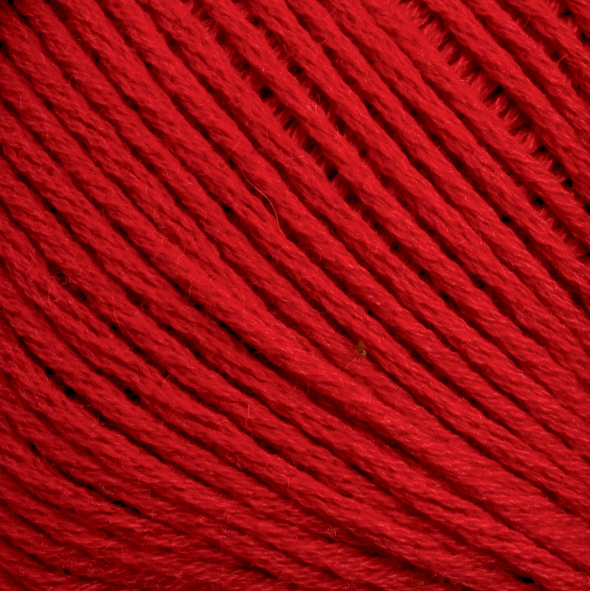 Close-up image of Cotton Fleece yarn by Brown Sheep. The red cotton yarn is densely wound, with individual fibers visible, highlighting its texture and vibrant color—perfect for intricate knitting patterns.