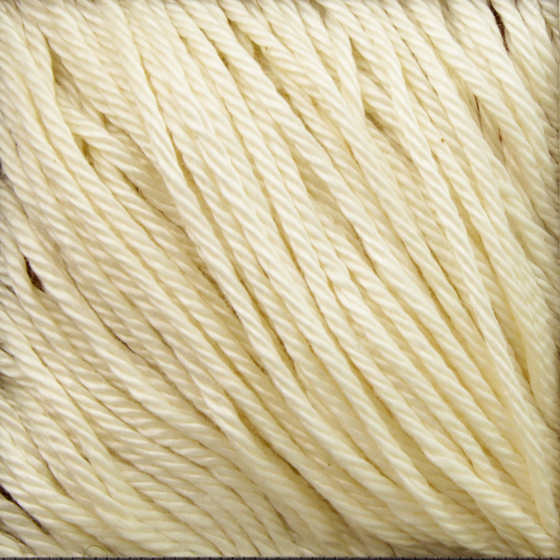 Close-up image of cream-colored yarn made from Cascade Ultra Pima Cotton Yarn by Cascade Yarns. The yarn is neatly wound into parallel strands, showcasing its soft texture and subtle sheen. The individual threads are tightly twisted, suggesting a high-quality, durable material suitable for knitting or crocheting.