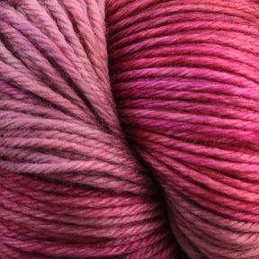 A close-up of a skein of Malabrigo Yarn's Malabrigo Arroyo highlights its smooth and tightly wound texture in shades of pink and purple. The gradient transitions beautifully from light pink to deeper magenta and purple hues, making it the perfect sport weight superwash merino wool yarn for creating lightweight garments.