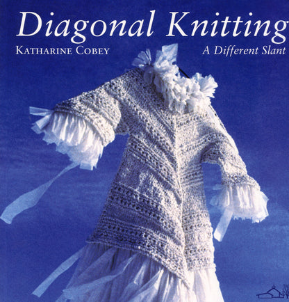 Cover image of the book "Diagonal Knitting" by Katharine Cobey, published by Schoolhouse Press. The scene features a knitted garment with ruffled sleeves and flowing, white fabric set against a blue sky. The title is written in white at the top, accompanied by the author's name and the subtitle, "A Different Slant.