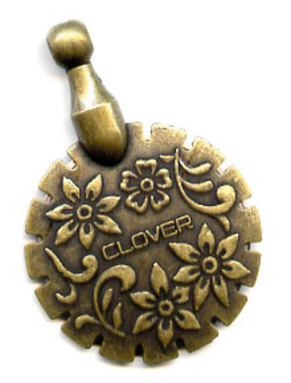 The Thread Cutter Pendant by Bryson Distributing, Inc. features a bronze-colored, circular design adorned with intricate floral engravings and the word "CLOVER" at its center. The zinc pendant is highlighted by a textured, gear-like edge and detailed patterns of flowers and vines, topped with a small, looped handle.