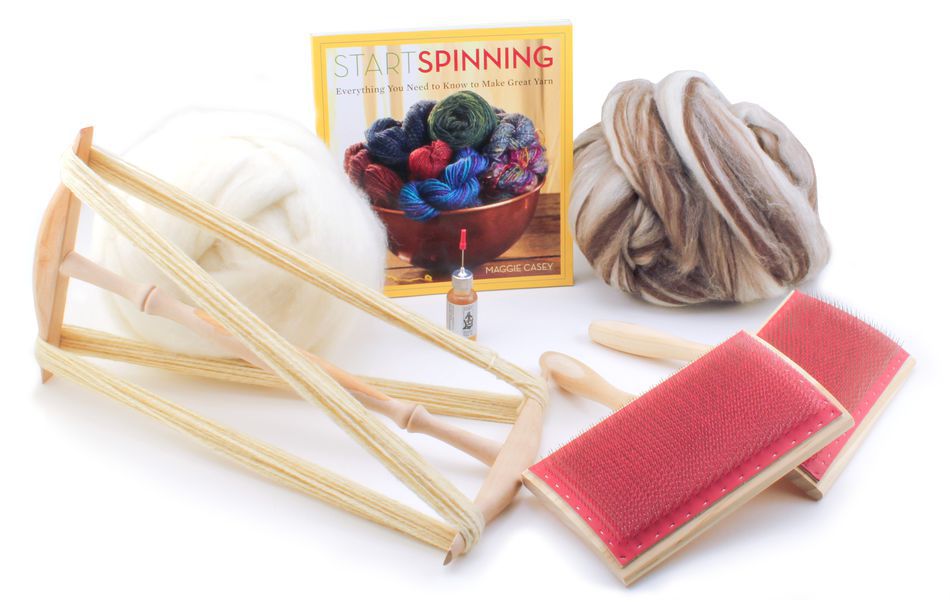 The Halcyon Yarn Quick-Start Spinning Accessory Package by Halcyon Yarn includes a "Start Spinning" book, a skein of white wool, a skein of brown and white wool, an Ashford hand carder with red pads, a spindle with spun yarn, and a small vial of oil.