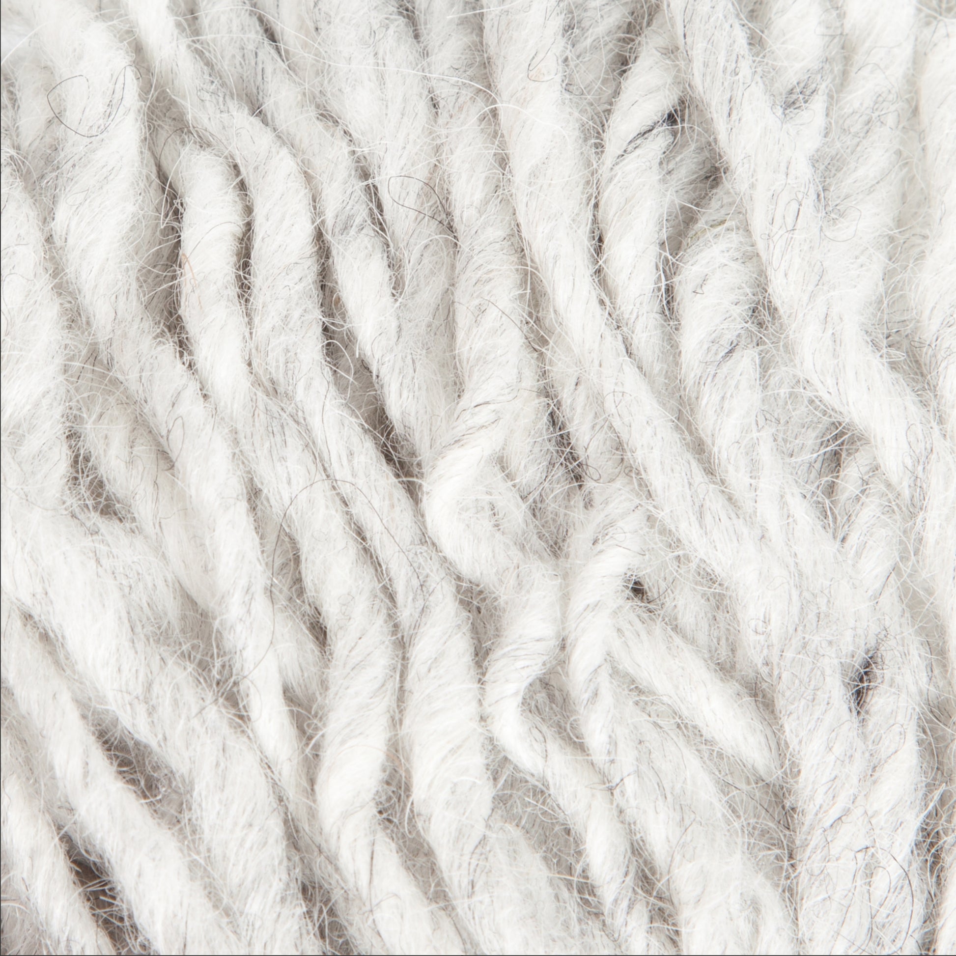 A close-up image of soft, thick strands of light gray Jöklalopi (Bulky Lopi) wool yarn by Berroco, Inc. The fibers are loosely spun, creating a textured and fluffy appearance that radiates rustic handmade charm. The natural colors make this cozy Jöklalopi yarn perfect for crafting chunky winter sweaters.