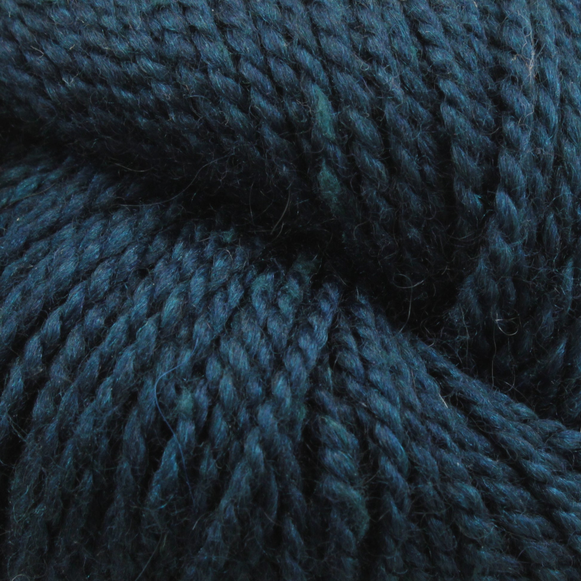 Close-up image of dark teal twisted Acadia yarn by The Fibre Co. (UK) Ltd. The texture reveals intricate strands tightly wound together, with a subtle tweed effect that highlights the soft and fibrous nature of the yarn. The deep color and detailed twists give the image a rich, tactile appearance.