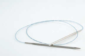 A pair of Skacel Addi Turbo Circular Knitting Needles connected by a flexible blue cable is shown against a plain white background. The smooth, reflective needles are ideal for knitting cuffs, collars, and doll clothes, with measurement markings along the cable ensuring precision.