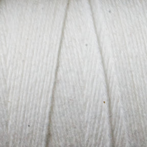 Close-up image of Maurice Brassard's Cotton 8/8 Carpet Warp. The texture is clearly visible, showcasing the soft fibers twisted together. Made of unmercerized cotton, the yarn exhibits a slightly fuzzy appearance with small individual strands intertwining to form a thick, cohesive thread perfect for knitting and crochet projects.