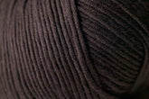 Close-up view of a ball of dark gray Jo Sharp Soho Summer DK Cotton Yarn from Kingfisher Yarn & Fibre. The image captures the texture and details of the tightly wound fibers, highlighting the soft and thick quality of this lightweight cotton yarn perfect for summer projects.