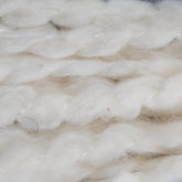 Close-up of twisted, fluffy, white wool fibers from Tess Cotton Yarn by Henry's Attic. The image shows soft and loose strands with a slightly shiny texture, creating a sense of warmth and softness. Ideal for knitting baby blankets or using in cotton roving projects, the fibers are intricately intertwined, giving a tactile and cozy appearance.