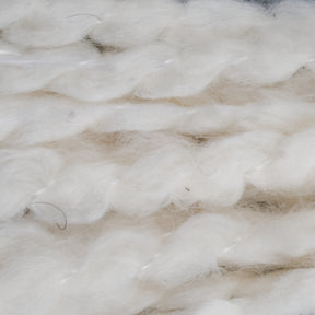 Close-up of twisted, fluffy, white wool fibers from Tess Cotton Yarn by Henry's Attic. The image shows soft and loose strands with a slightly shiny texture, creating a sense of warmth and softness. Ideal for knitting baby blankets or using in cotton roving projects, the fibers are intricately intertwined, giving a tactile and cozy appearance.