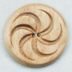 The Wood Button by Alosada is a round, light brown wooden button featuring a carved swirling design akin to a pinwheel, with two central holes for threading. Made from all-natural local materials, it boasts a smooth, polished finish that highlights the craftsmanship of Alosada LLC's hand-carved buttons.