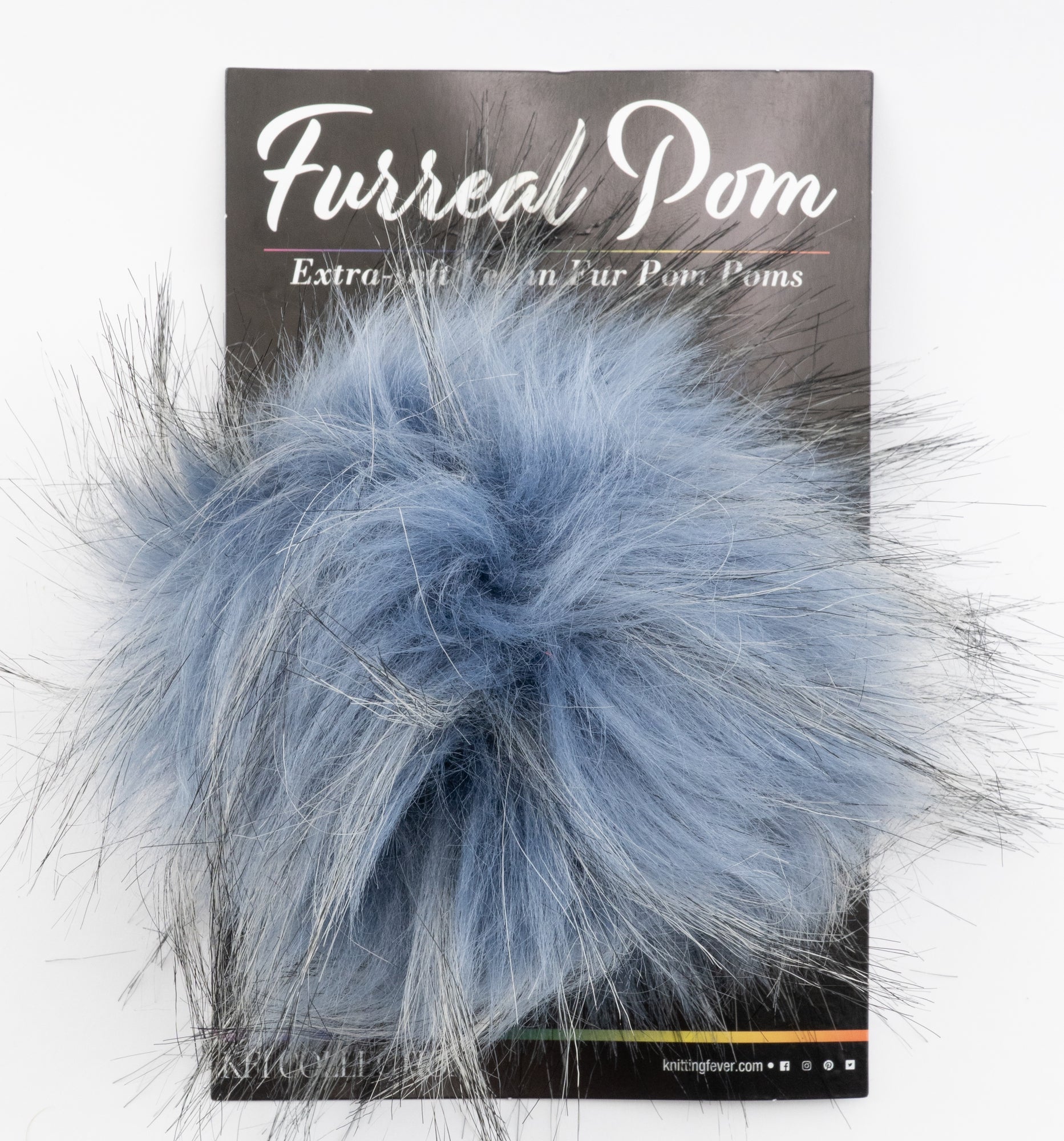 A package with a fluffy faux fur pom-pom attached, primarily light blue with some strands of white and black mixed in. The packaging reads "Furreal Pom by KFI" at the top, from the brand Knitting Fever / Euro Yarns.