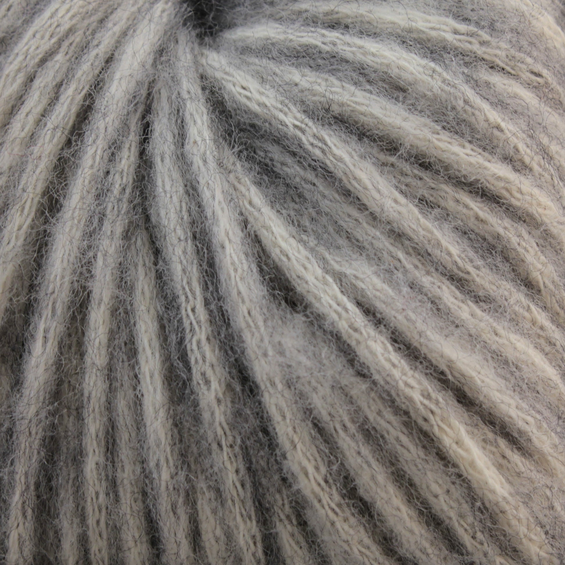 Close-up of Katia Cotton-Merino yarn by Knitting Fever / Euro Yarns, showing a detailed view of its gray and white twisted fibers. The yarn strands are closely packed, creating a textured and soft appearance. The colors blend subtly, showcasing a mix of light and dark shades in this fine cotton-Merino wool blend.