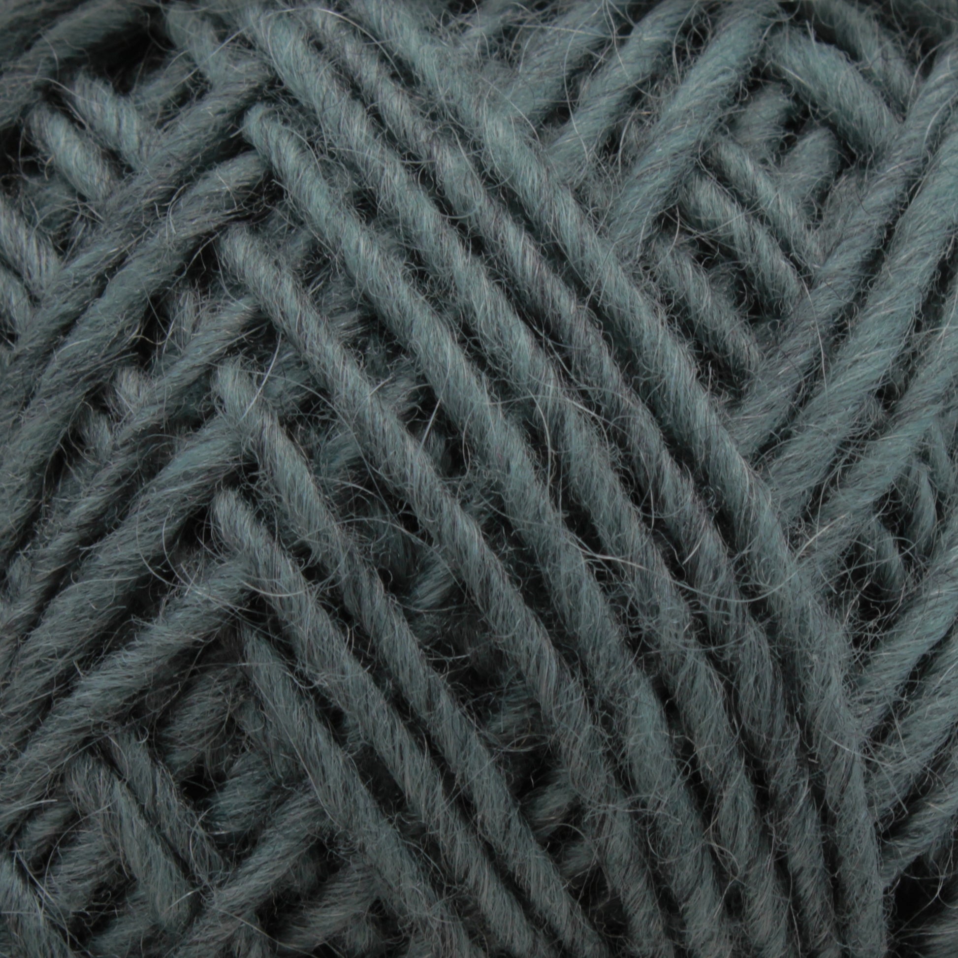 Close-up of a ball of yarn in a soft, muted green color. The Lamb's Pride Worsted Yarn by Brown Sheep reveals its texture, showcasing the individual strands tightly wound together. This image highlights the detail and coziness of the material, making it an ideal choice for felting projects or Navajo-style weaving.