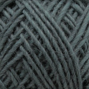 Close-up of a ball of yarn in a soft, muted green color. The Lamb's Pride Worsted Yarn by Brown Sheep reveals its texture, showcasing the individual strands tightly wound together. This image highlights the detail and coziness of the material, making it an ideal choice for felting projects or Navajo-style weaving.