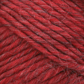 Close-up of Lamb's Pride Bulky Yarn in red showing detailed texture, perfect for knitters and crocheters. The yarn, from the Brown Sheep brand, consists of tightly twisted strands with some white fibers intertwined, creating a slightly variegated appearance. The image highlights the fibers and twists, offering a rich, textured surface.