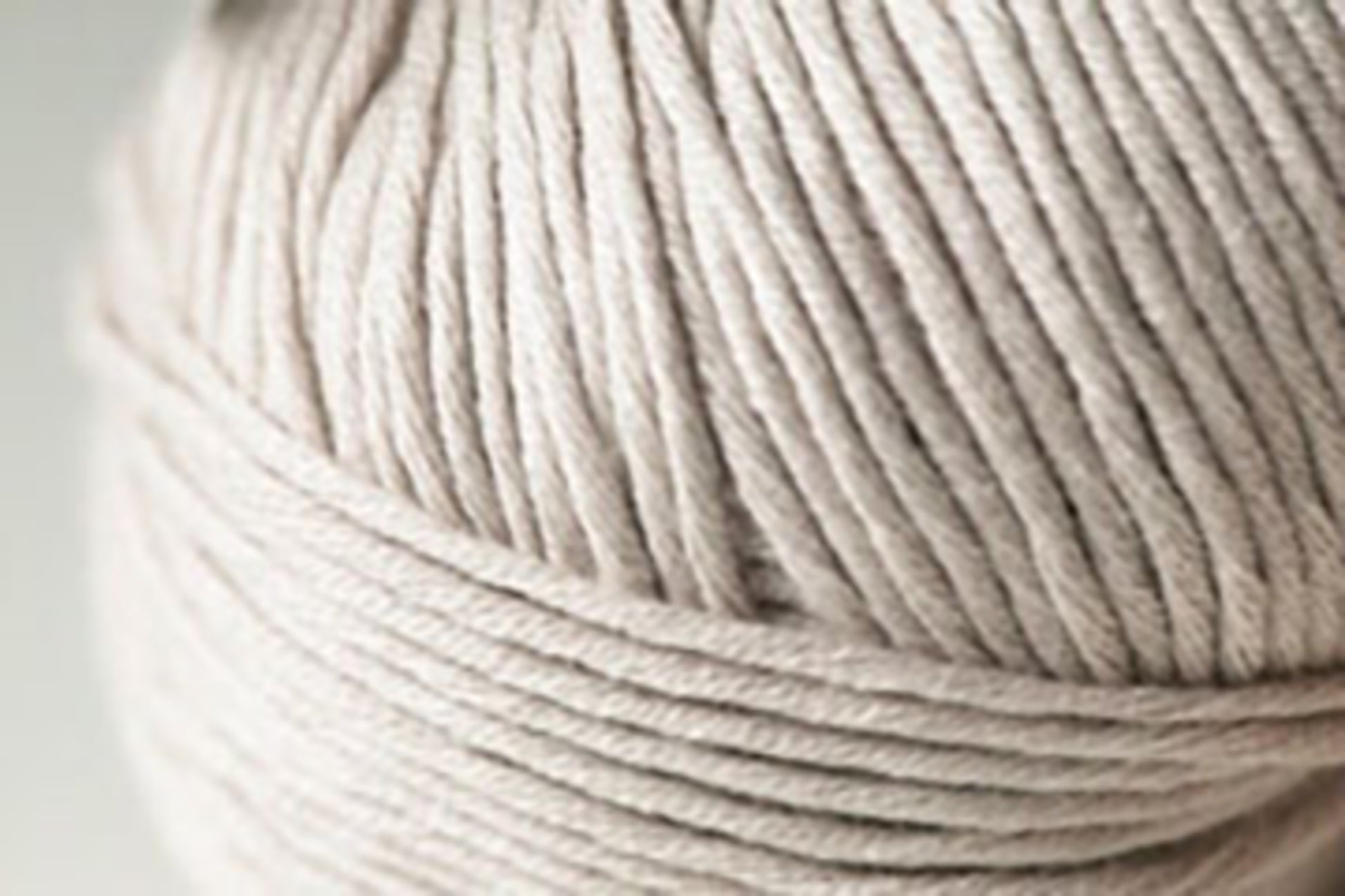 A close-up of a ball of Kingfisher Yarn & Fibre's Jo Sharp Soho Summer DK Cotton with tightly wound fibers, showing detailed texture. The yarn appears soft and smooth, perfect for summer knitting or crocheting projects. The background is blurred, drawing focus to the lightweight cotton yarn.