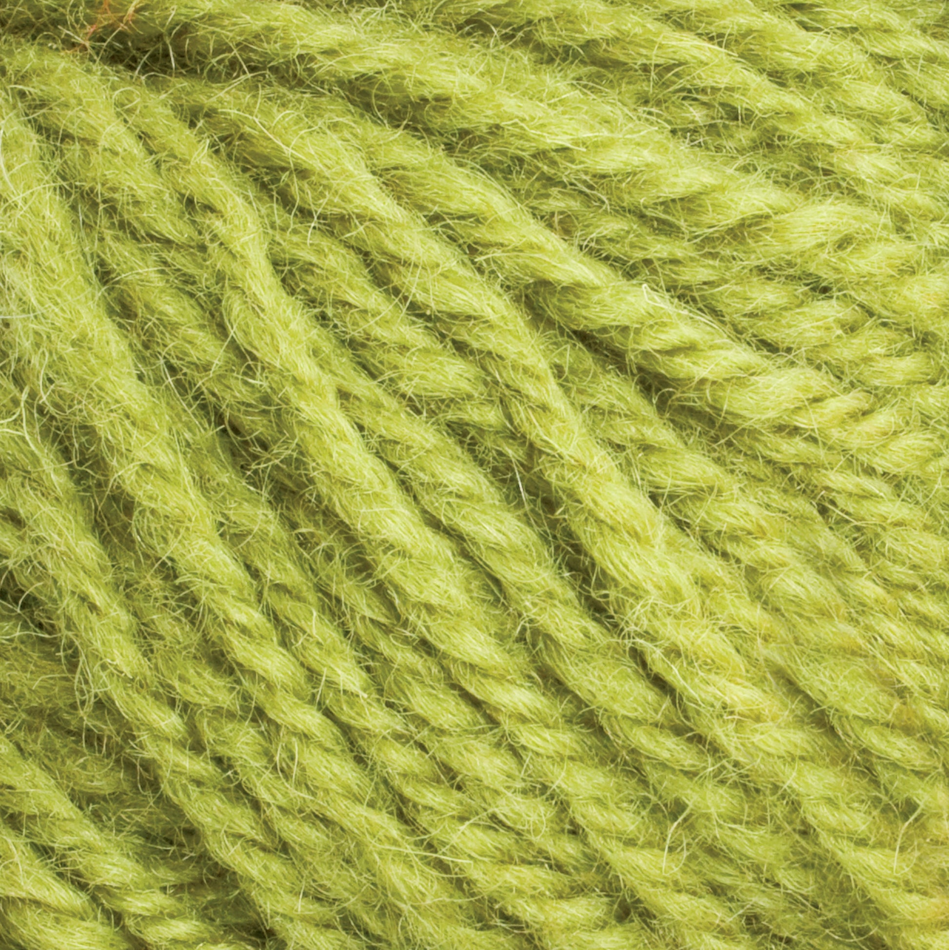 Close-up of the light green Halcyon Deco Rug Wool from Caledonian Dye Works, made from 100% wool with a soft and fuzzy texture. The yarn is tightly twisted and features variations in thickness and color, contributing to its depth and natural appearance. This versatile yarn is perfect for creating unique projects.