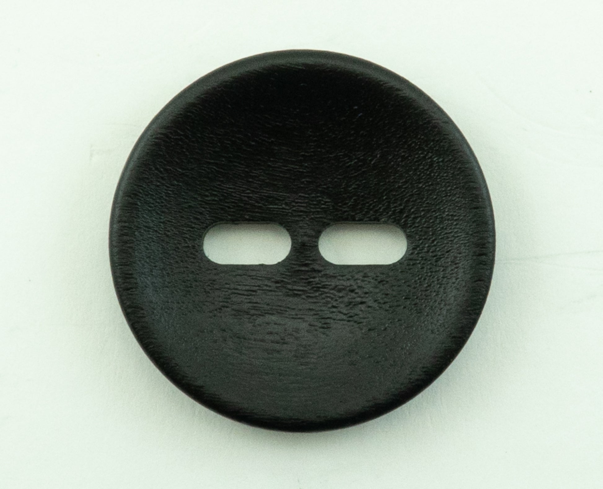 A close-up photo of the "Wood Foxeye" by Buttons Etc., a black, round wooden button with a 1 3/8" diameter, against a plain white background. The button has a smooth texture and lies flat, with its two elongated holes positioned horizontally in the center.