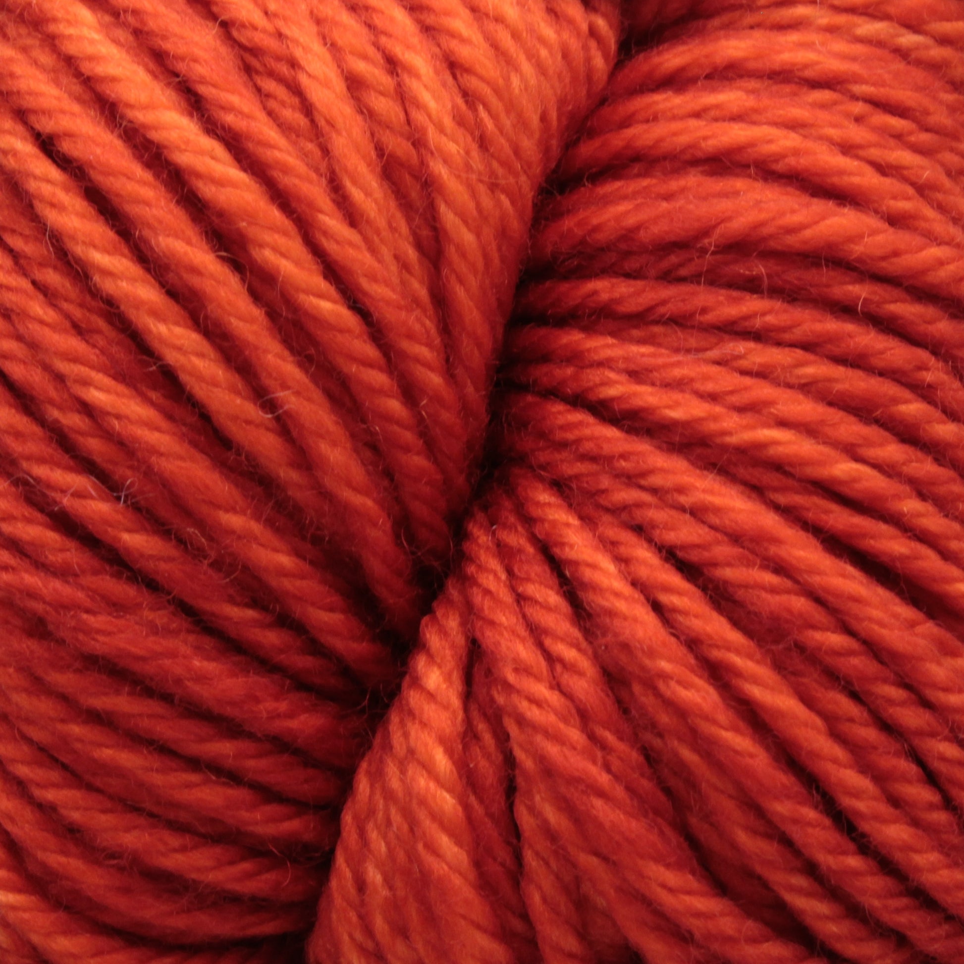 Close-up image of tightly wound, soft Malabrigo Rios yarn by Malabrigo Yarn in rich shades of orange. The texture is clear, showing the twist and individual fibers of the superwash yarn, creating a warm and cozy appearance.