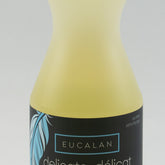 The Eucalan Wool Wash 16.9 oz bottle, enriched with lanolin, features a black label with text in both English and French that reads "delicate - délicat" and "unscented - non parfumée." The yellow bottle, capped with black and adorned with a blue feather design, is also 100% biodegradable.