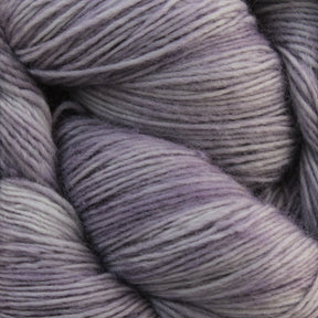 Close-up image of skeins of Malabrigo Lace yarn by Malabrigo Yarn in shades of gray and lavender, highlighting the intricate fibers and smooth textures. The colors blend seamlessly, creating a gradient effect. The thick and cozy merino wool yarn is ideal for knitting or crocheting projects like knitted shawls.