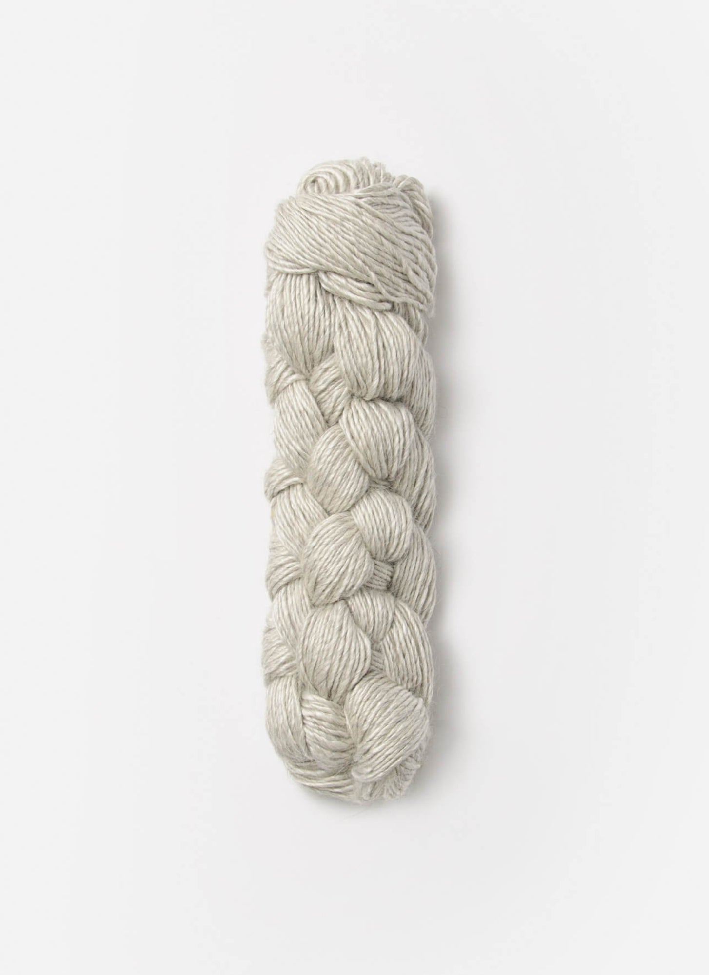 A neatly twisted skein of Blue Sky Fibers Metalico sport weight yarn in light gray rests against a plain white background. The Blue Sky Fibers silk blend yarn is intertwined in a braided, cylindrical shape, showcasing a smooth and consistent texture.