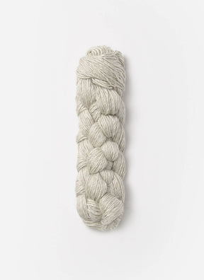 A neatly twisted skein of Blue Sky Fibers Metalico sport weight yarn in light gray rests against a plain white background. The Blue Sky Fibers silk blend yarn is intertwined in a braided, cylindrical shape, showcasing a smooth and consistent texture.