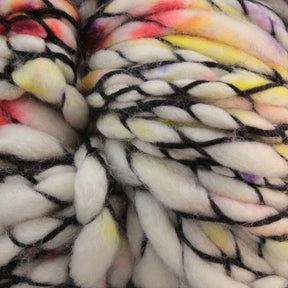 Close-up of Malabrigo Caracol, a thick, multicolored super bulky yarn by Malabrigo Yarn, featuring a mainly white base intertwined with black strands and vibrant splashes of red, orange, yellow, and purple throughout. The texture appears soft and fluffy, showcasing the luxurious quality of its kettle-dyed superwash merino wool.