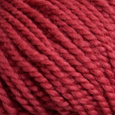 Close-up of a textured, thick red yarn. Norumbega by Caledonian Dye Works is an Aran weight yarn that is tightly twisted, creating a detailed, braided pattern. Made from 100% U.S. wool, the fibers appear soft and fluffy, highlighting the yarn’s cozy and warm characteristics suitable for knitting or crocheting.