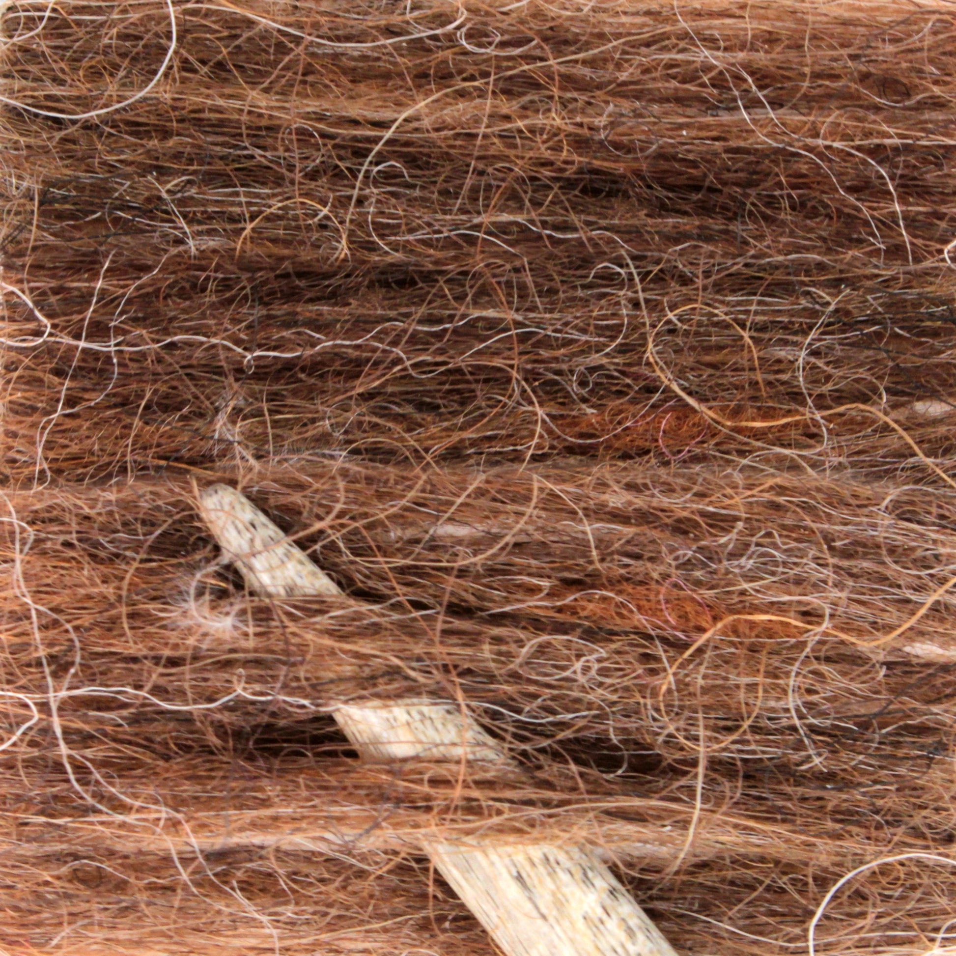 A close-up of a bundle of brown alpaca yarn with white fibers textured throughout. A wooden knitting needle is partially visible, nestled into the soft, fibrous yarn, possibly in use for knitting. The texture mirrors the charm of Plötulopi Unspun Icelandic Wool Yarn by Berroco, Inc., beautifully combining alpaca and Icelandic wool.