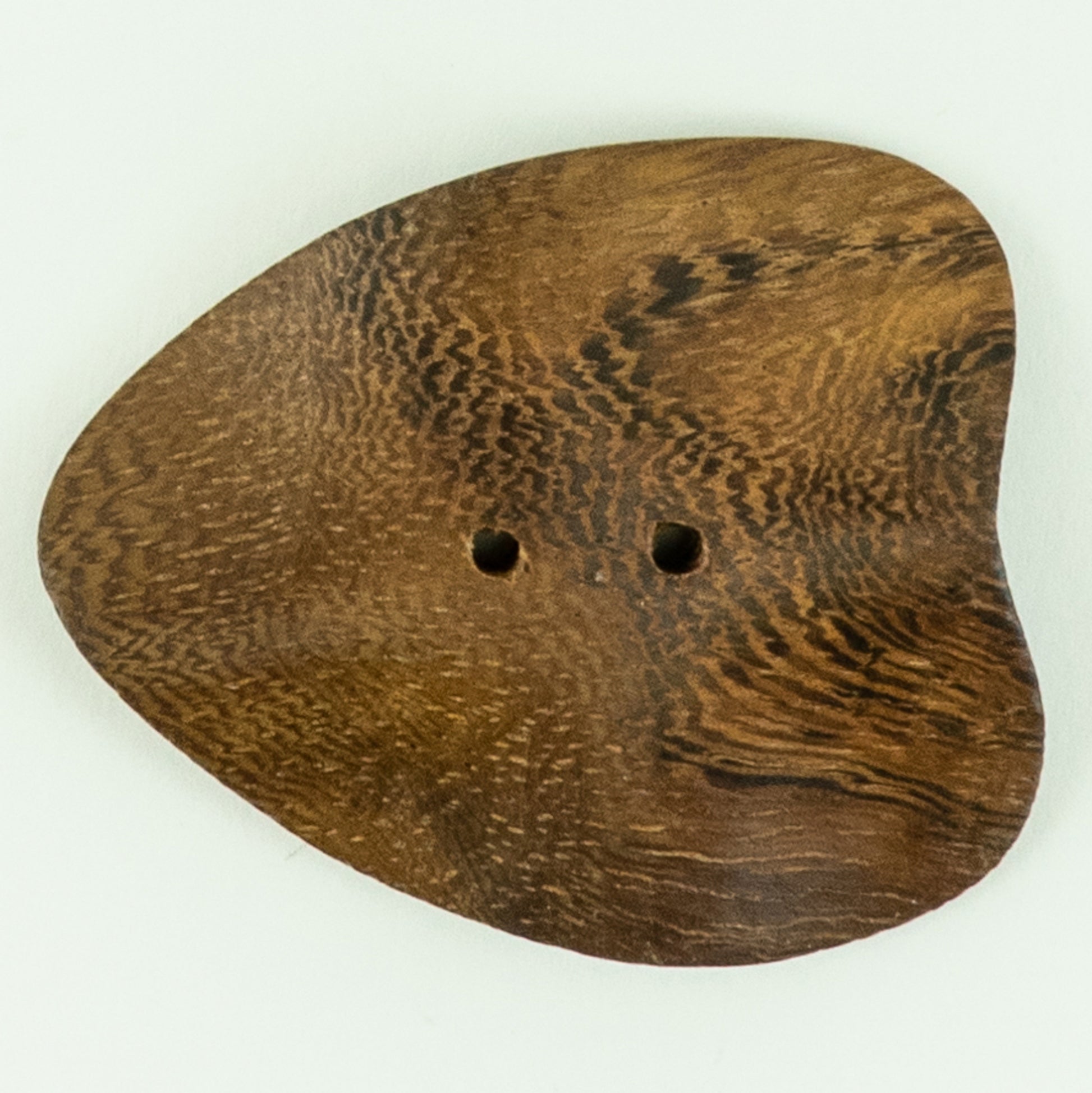 The Roble Wood Freeform Button from Buttons Etc. is a uniquely shaped, flat, brown wooden button with two holes in the center. Measuring 2 1/8" in diameter, it features a rich, textured wood grain pattern on its surface and resembles a rounded triangular or organic leaf form.