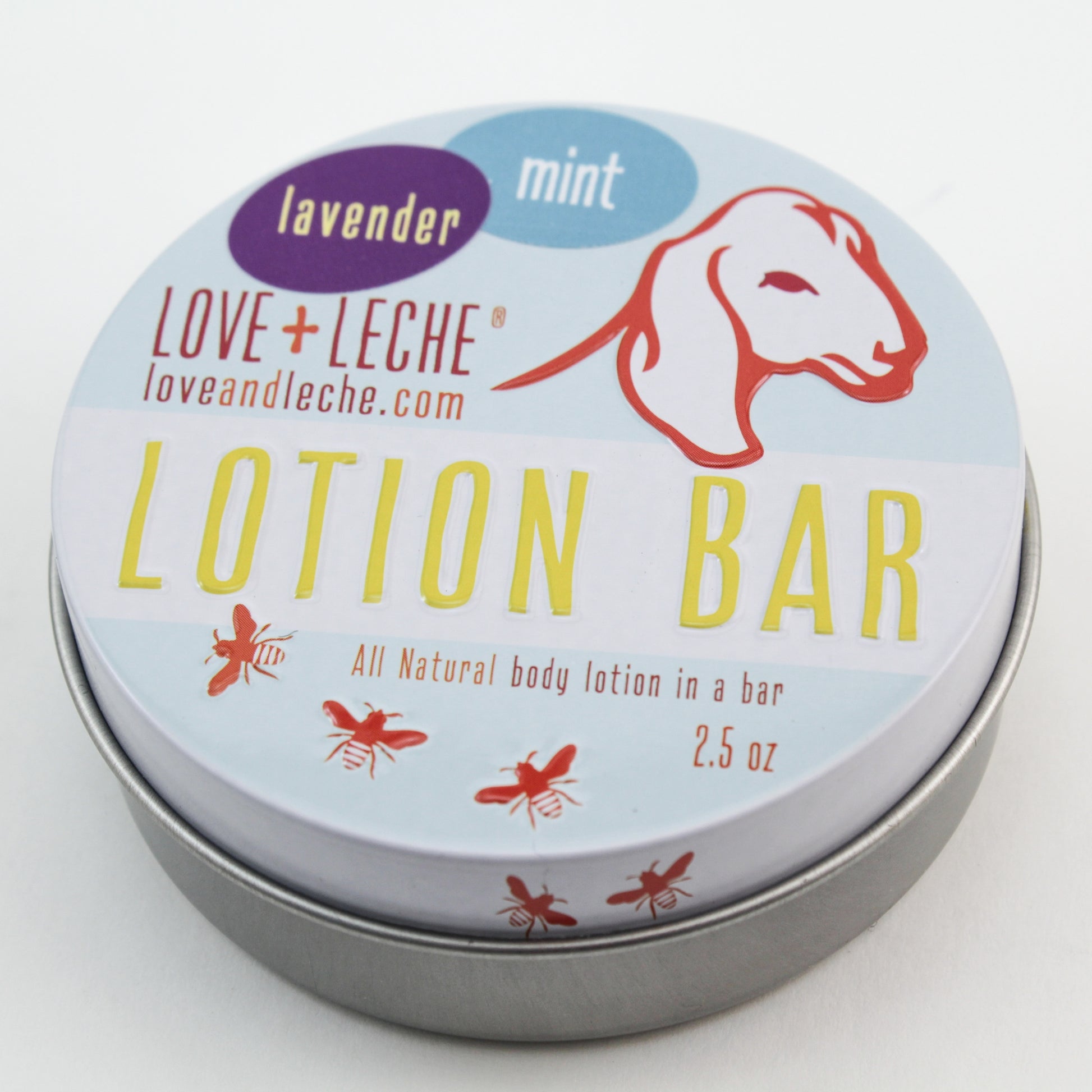 A silver tin containing a Love + Leche Lotion Bar, adorned with a label that reads "LOVE + LECHE, lavender, mint." The label is decorated with an illustration of a goat's head and the text "All natural body lotion in a bar, 2.5 oz" to highlight its premium quality. Crafted with nourishing beeswax for moisturized skin, small bee illustrations are charmingly scattered across the label.