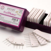 A purple box labeled "Knit Blockers by Knitter's Pride" from Accessories Unlimited sits open, revealing rows of white blockers with multiple pins. Additional knit blockers are arranged on blocking mats in front of the box, and the contents description on the label is partially visible.