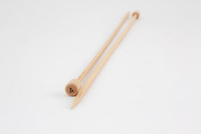 A pair of light wooden, 12" bamboo knitting needles from Accessories Unlimited, featuring pointed tips and rounded ends. One needle is clearly marked with the number 4 on its end. These Bamboo Single-Point Knitting Needles are placed parallel to each other on a white surface.