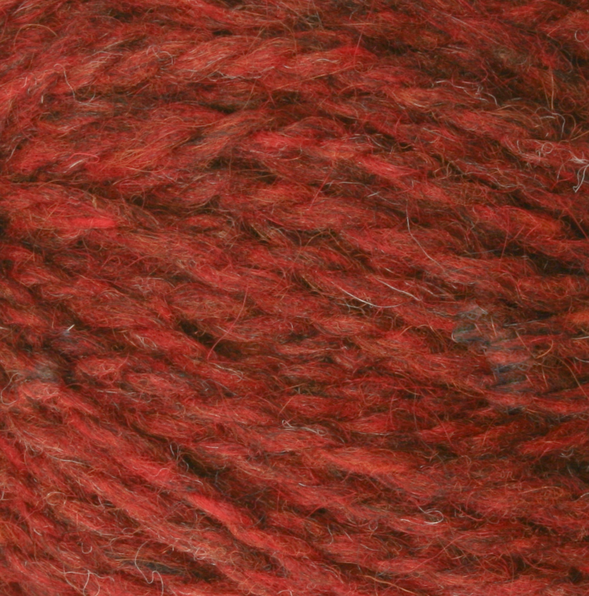 Close-up image of a ball of Peace Fleece Yarn by Harrisville Designs. The yarn appears to have a mixed texture with shades of red ranging from bright to dark, and it looks soft and woolly. This yarn is a wool and mohair blend, making it ideal for worsted weight knitting projects.