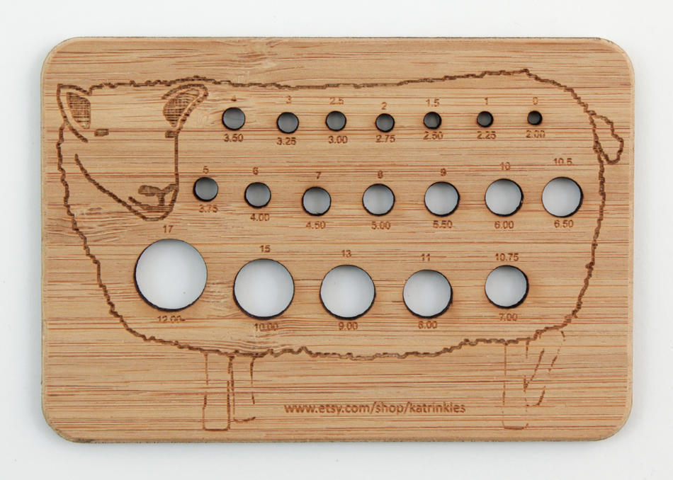 The Animal Needle Gauge from Never Not Knitting is a rectangular, laser-cut bamboo tool adorned with a delightful sheep design. It features circular holes in various sizes for measuring knitting needle diameters from 1.50 mm to 17.00 mm, with "www.etsy.com/shop/katrinkles" etched at the bottom.