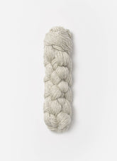 A neatly braided bundle of Blue Sky Fibers Metalico yarn in a light gray silk blend lies against a plain white background. The texture and tightness of the braiding are clearly visible, showcasing Blue Sky Fibers' fibrous material's smooth and slightly shiny surface.