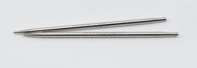 Two Nova Platina Interchangeable Knitting Needle tips from Accessories Unlimited, each 4.5 inches long and resembling slender hollow brass pipes, are laid parallel to each other on a white background. Each tip features a pointed end designed for insertion into the body of a knitting needle. The tips appear new and unused, like interchangeable components from Knitter's Pride Nova collection.