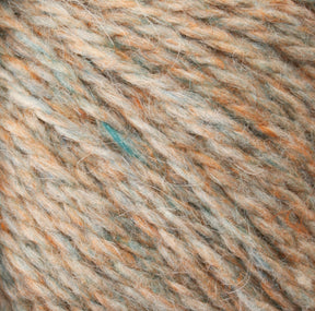 Close-up of a skein of Harrisville Designs' Peace Fleece Yarn, showcasing a mix of predominantly light brown and orange hues, accented with hints of blue and green. The texture appears soft and slightly fluffy, indicating a wool and mohair blend that is ideal for worsted weight knitting projects.