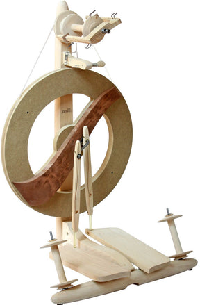 The Kromski Fantasia Spinning Wheel by Kromski North America is a wooden spinning wheel with a large circular frame and foot pedal mechanism. It boasts an elegant design that combines light and dark wood, showcasing detailed craftsmanship. This modern double drive wheel features Kromski bobbins and a flyer for expertly spinning fibers into yarn.