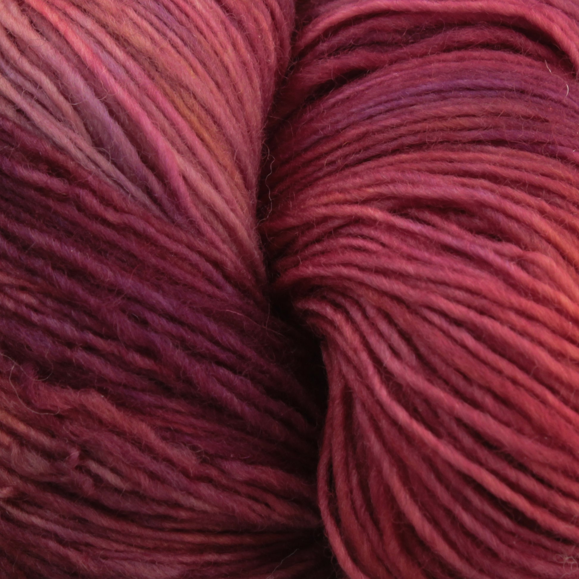 Close-up of a skein of Malabrigo Lace by Malabrigo Yarn in shades of red and burgundy. The yarn strands are tightly wound together, creating a rich texture with subtle variations in color throughout, perfect for crafting elegant knitted shawls.