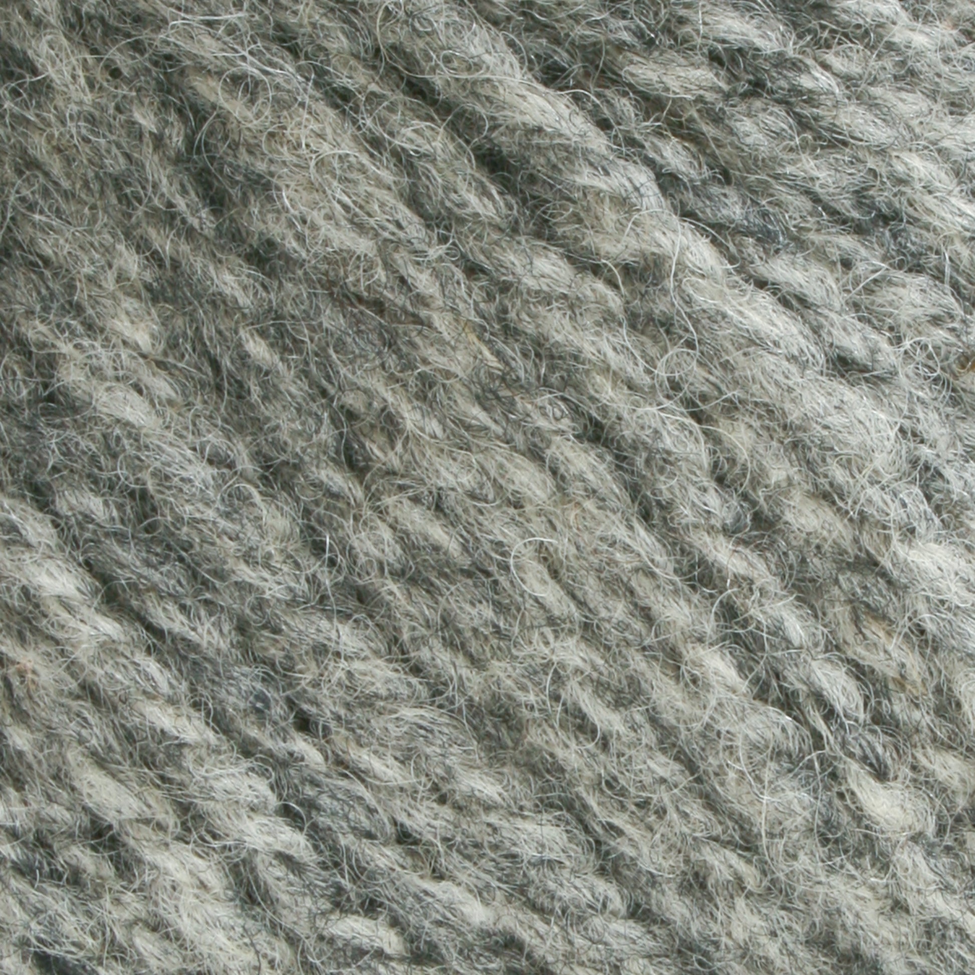 Close-up of Bartlettyarns Maine Wool Yarn with visible fibers. The thick, slightly fuzzy material suggests it could be used for knitting or crocheting projects. This worsted weight yarn from Bartlettyarns boasts a coarse, heathered look with variations in gray tones.