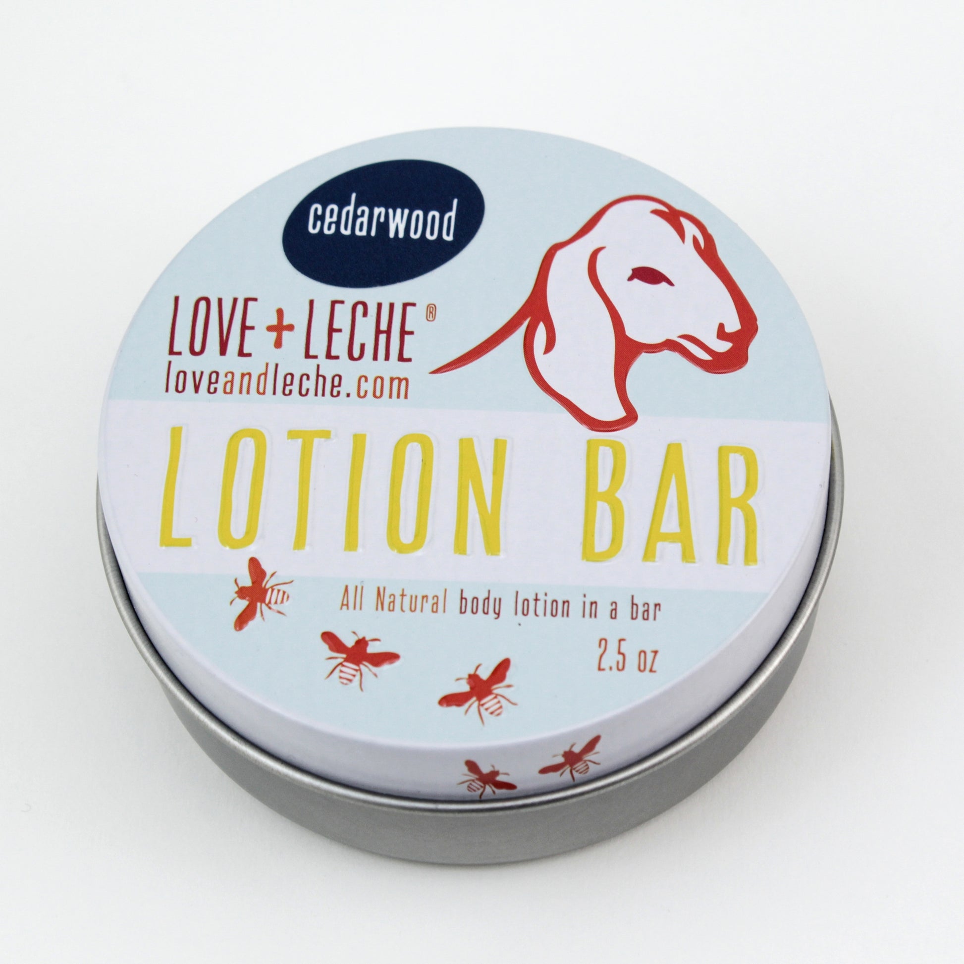 A tin container labeled "Love + Leche Lotion Bar," featuring a graphic of a goat's head and text reading "Cedarwood," "loveandleche.com," and "Lotion Bar," proudly showcases its beeswax-based formula. The text also states, "All Natural body lotion in a bar" and "2.5 oz." Small illustrations of bees surround the container.