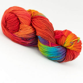 A hank of Great Adirondack Organic DK Cotton yarn from Great Adirondack Yarn Co, Inc. is displayed against a white background. The hand-dyed yarn transitions through various shades including red, orange, yellow, green, blue, and purple, creating a vibrant and visually appealing spectrum.