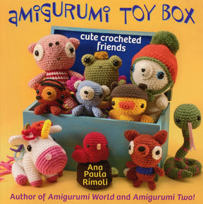 Cover of the "Amigurumi Toy Box" book by Ana Paula Rimoli, published by Martingale & Co. The image showcases a delightful collection of colorful, easy-to-make crocheted animal toys such as a bear, frog, bird, deer, and others arranged in and around a blue toy box. The text on the cover reads "cute crocheted friends".