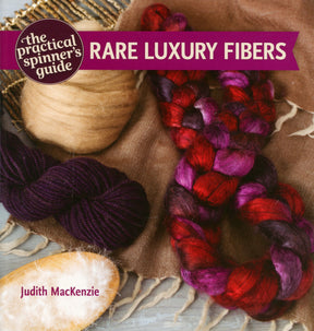 The image displays the book cover for "The Practical Spinner's Guide Rare Luxury Fibers" by Judith MacKenzie, published by Ingram Content. It showcases an array of fibers in both natural and dyed colors, including a dark purple skein and braids in shades of purple and red, all arranged on brown fabric. The cover hints at the advanced spinning techniques featured within the book.