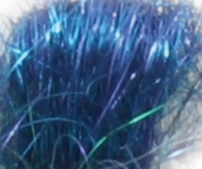 A close-up view of a bundle of Crystal Mylar Fiber by Foxglove Fiberarts Supply showcases densely packed, dark blue synthetic fibers with hints of green and purple iridescence, giving it a glossy and slightly tangled appearance. The novelty yarns create a shiny, textured surface adorned with shimmering highlights.